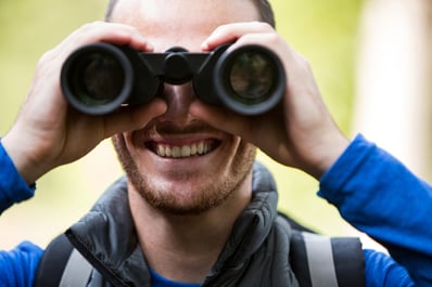 Close-up of male hiker looking through binoculars in forest